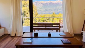 Une pièce avec une table en bois, deux chaises et une vue sur les montagnes, visible à travers une porte vitrée.