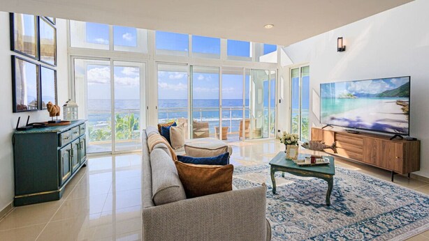 A spacious living room with a large TV, a sofa, and a coffee table. - Stunning Beach Front 5BD Penthouse, Spectacular Sea Views (Playa Juan Dolio)