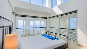 A bedroom with a bed, a nightstand, a lamp, and large windows with a view of the sea. - Stunning Beach Front 5BD Penthouse, Spectacular Sea Views (Playa Juan Dolio)