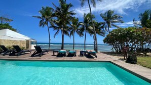 A poolside area with lounge chairs, a pool, palm trees, and a view of the ocean. - Stunning Beach Front 5BD Penthouse, Spectacular Sea Views (Playa Juan Dolio)