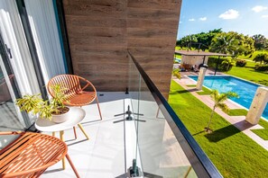 Ein Balkon mit Glasgeländer, einem Holztisch, zwei Stühlen und Topfpflanzen.