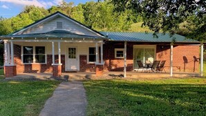 A two-story brick house with a covered porch and a separate garage. - Private 16-Acre Escape w/ Creek • Peaceful & Quiet • Fire Pit, Hiking & Lake (Hampton)