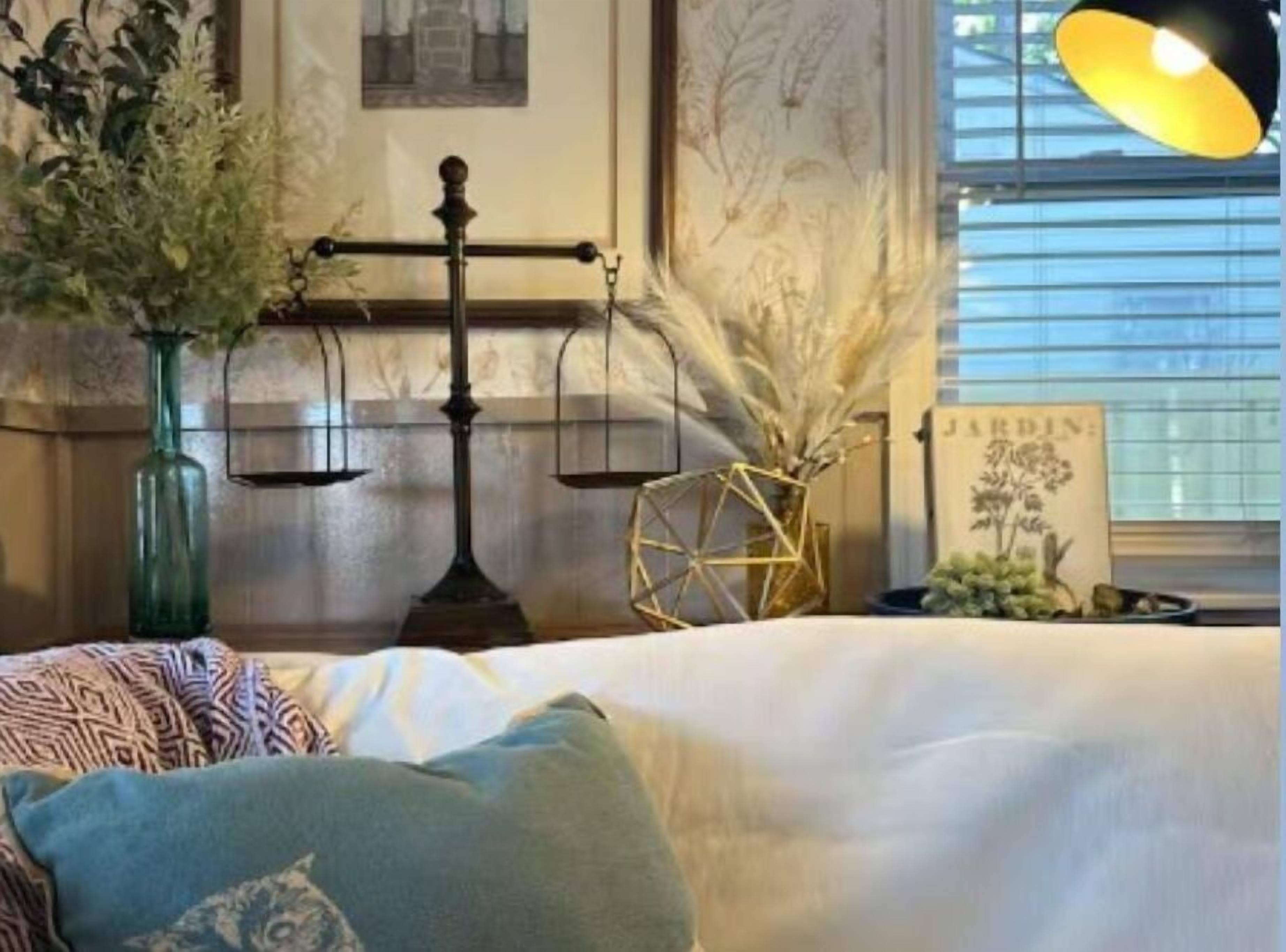 Ein Zimmer mit einem Bett, einer Wandwaage, einem gerahmten Bild und einem Fenster mit Jalousien.