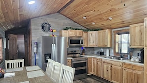 Eine Küche mit Holzschränken, einem Edelstahlkühlschrank, einer Mikrowelle und einem Essbereich mit Tisch und Stühlen.