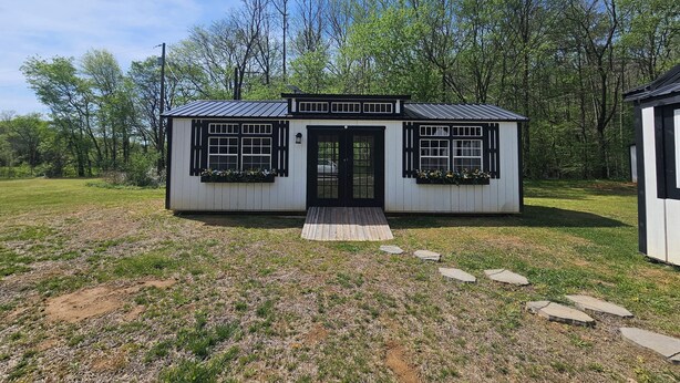 Une petite cabane à un seul étage, dotée d’un porche à l’avant, de fenêtres à cadre noir et d’un toit en métal.