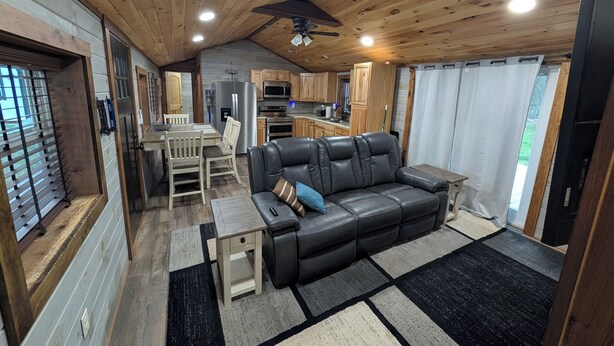 Ein Interieur einer Hütte mit Essbereich, einer schwarzen Ledersofa, einer Küche und einem Deckenventilator.