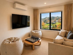 A living room with a flat-screen TV, a chessboard, and a sofa. - SAKURA LODGE in Daylesford Victoria (Daylesford)