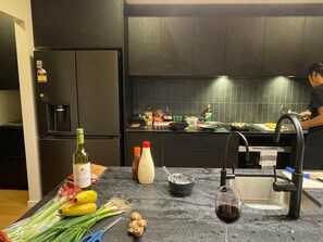 Una cocina con un refrigerador, un lavamanos y diversos alimentos sobre la encimera.