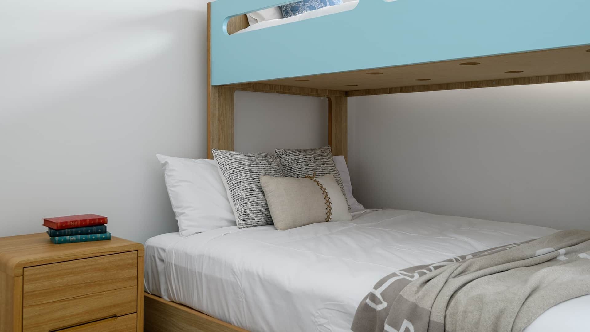 Una cama litera con ropa de cama blanca, una mesita de noche de madera con libros y un cabecero azul.