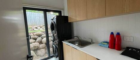 Una cocina con armarios de madera, un lavamanos de acero inoxidable y un portón de vidrio que da a un espacio exterior con rocas y una valla.