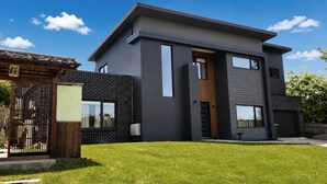 Une maison moderne à deux étages, avec une façade en briques, un portail en bois et une pelouse bien entretenue.