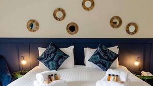 Habitación de hotel con cama, dos almohadas, cabecero, espejos montados en la pared y mesita de noche con lámpara.