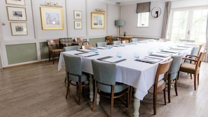 Un salón de conferencias con una larga mesa, sillas, cuadros en la pared y una lámpara.