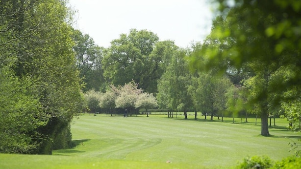 Campo de golf con césped cuidado, árboles y cielo despejado.