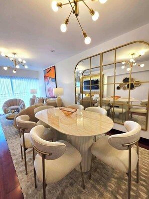 A modern living room with a round marble table, comfortable seating, a large mirror, and a television. - Miraflores Luxury Skytop Oceanview Apartment (Miraflores)