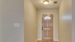 Un couloir avec une porte en bois, un interrupteur et un luminaire au plafond.