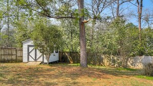 Une cour arrière avec un abri en bois, un arbre et une clôture.
