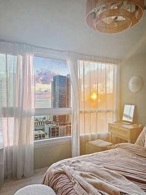 A bedroom with a large window, a bed, a desk, and a chair. - Sea to Sky Corner Penthouse Ocean and Diamond Head Views (Honolulu)