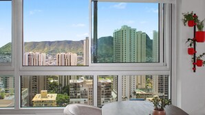 Ein Zimmer mit großen Fenstern und Blick auf umliegende Gebäude und Hügel.