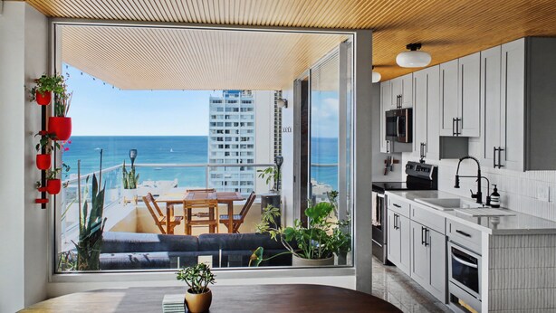 Eine moderne Küche mit Meerblick, ein Essbereich mit Tisch und Stühlen sowie ein Balkon mit Pflanzen und einer Couch.