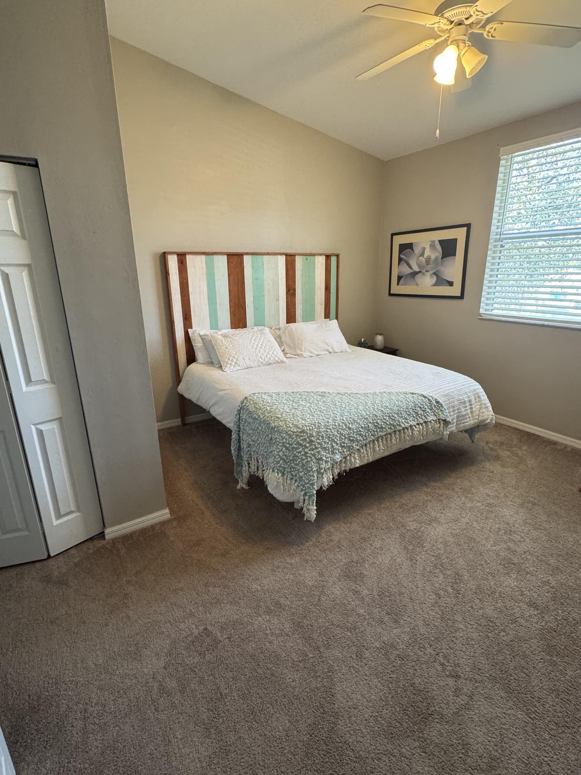 Une chambre à coucher avec un lit, un ventilateur de plafond, une fenêtre avec des stores et une porte.