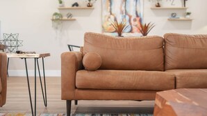 A brown leather sofa with a single cushion, a small wooden table with geometric decor, and a painting with guitars on the wall. - New Downtown Chandler | Family & Pet-Friendly (Chandler)