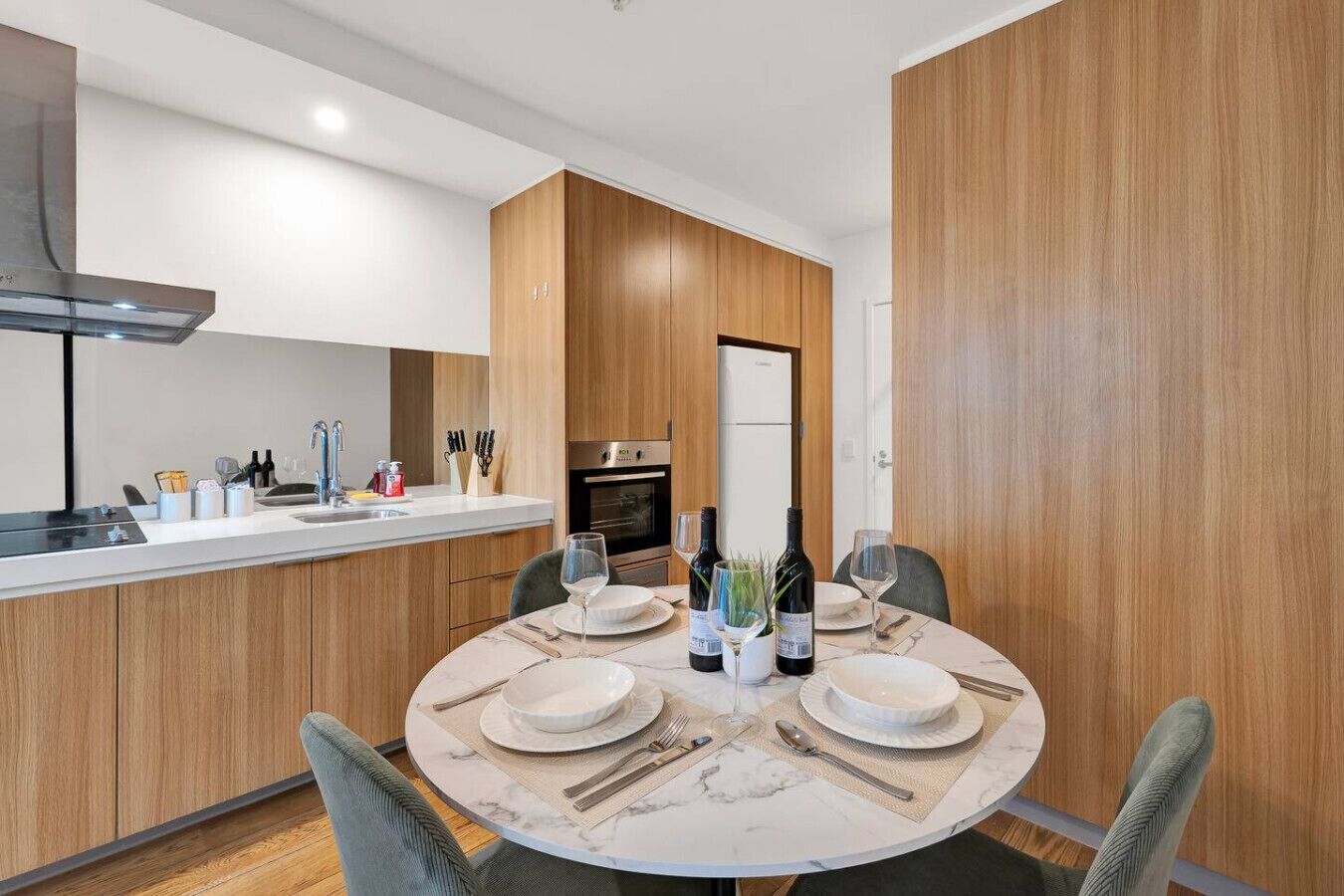 A modern kitchen with wooden cabinets, a built-in oven, and a dining area with a round table set for four.