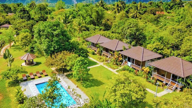 Un resort con varias edificaciones tipo bungaló, piscina y abundante vegetación.
