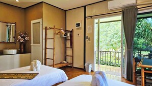 Una habitación de hotel con dos camas, un baño con lavamanos, un espejo, una escalera de madera, y un balcón con mesa y sillas.