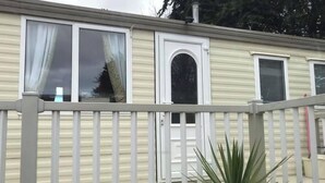 Ein Wohnmobil mit weißer Außenfarbe, einer Haustür mit rundem Fenster und einem Balkon mit Geländer.