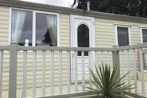 A mobile home with a white exterior, a front door with an arched window, and a balcony with a railing. - 14 South Happy Days - Sleeps 6 Pet free caravan (Skegness)