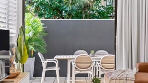 A modern living room with a dining area, white furniture, a TV, and a view of greenery.