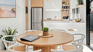 A modern kitchen with a central island, stainless steel appliances, and a dining area with white chairs and a wooden table.
