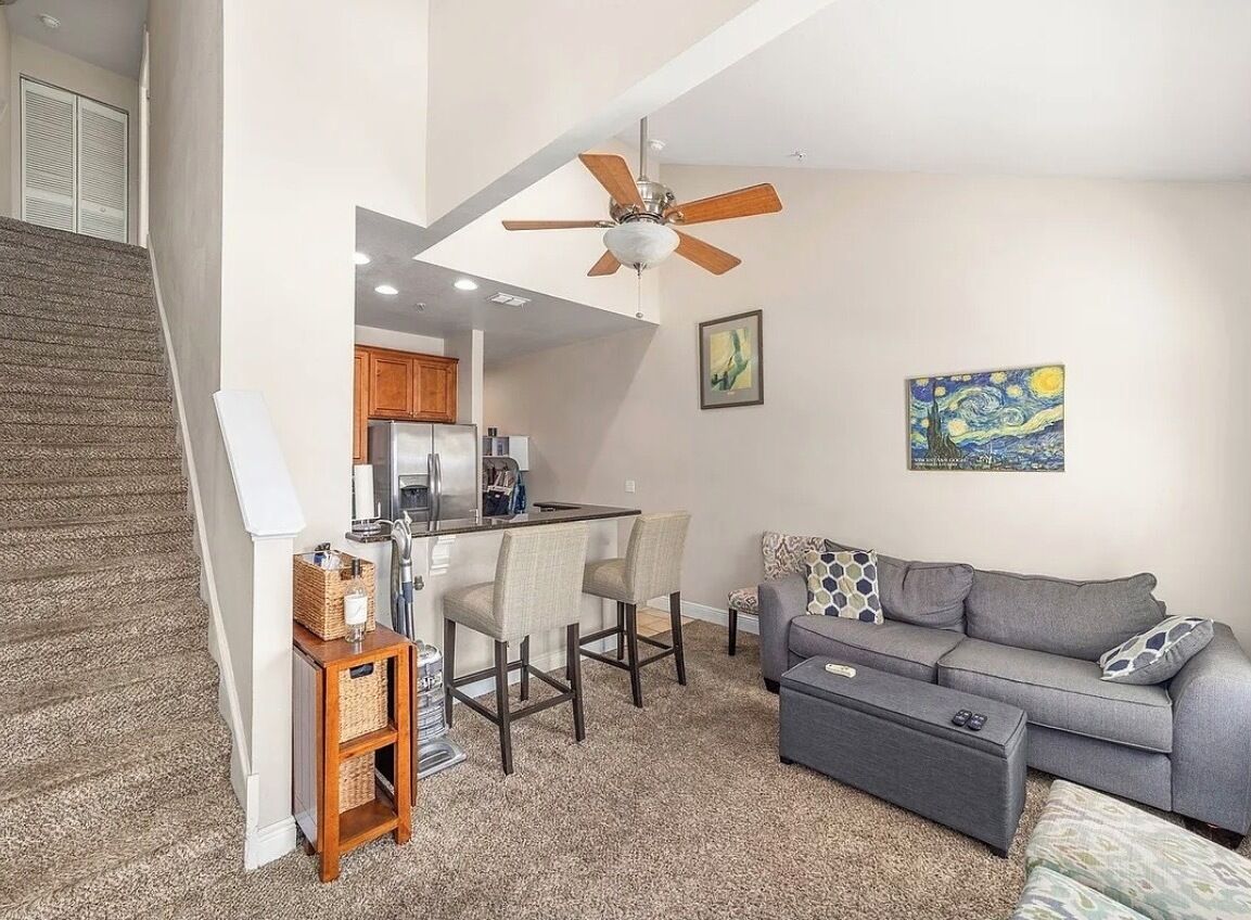A modern living space with a kitchen, dining area, and a gray sofa with patterned cushions.
