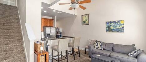 A modern living space with a kitchen, dining area, and a gray sofa with patterned cushions.