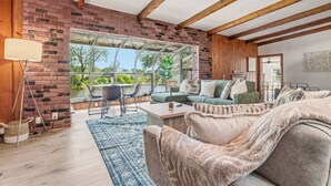 Un salon avec un mur en briques, des poutres apparentes, un canapé, une table basse et une vue sur la verdure à l’extérieur.