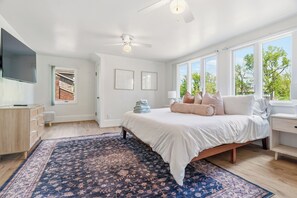 Une chambre à coucher avec un lit, un ventilateur de plafond, une télévision, une fenêtre et une porte.