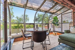 Een kamer met een glazen plafond, een ronde tafel, stoelen, een bank en uitzicht op groen en een rivier.