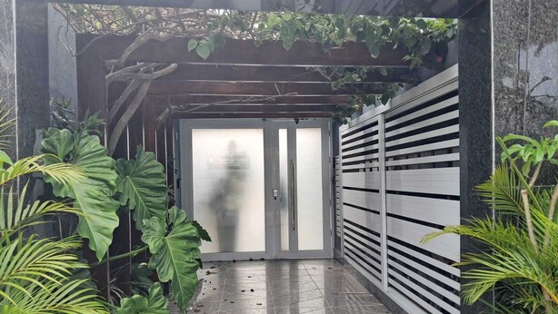 Une entrée abritée, dotée d’un portail en métal, de grandes plantes vertes et d’un sol carrelé.