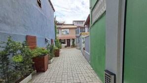 Une ruelle étroite, pavée de pierres, bordée de bâtiments aux styles architecturaux variés et agrémentée de quelques espaces verts.