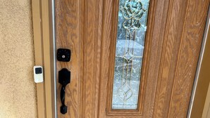 Une porte en bois avec un panneau de verre, un interphone et un clavier à code.