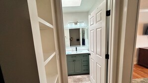 Un couloir menant à une salle de bain équipée d’un miroir, d’un lavabo et de placards.