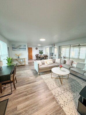 Ein geräumiges Wohnzimmer mit Essbereich, einer Sofagarnitur, einem Couchtisch und einem großen Fenster.