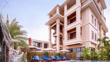 Un hotel con piscina, varios balcones y una cascada.