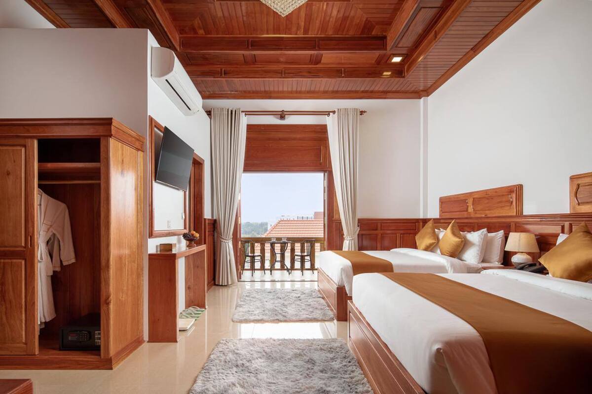 A hotel room with wooden ceiling, a balcony, a TV, a wardrobe, and two beds.