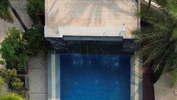 Une vue aérienne d’une piscine rectangulaire, où l’on aperçoit une personne flottant au centre, entourée de plantes en pot et de mobilier d’extérieur.