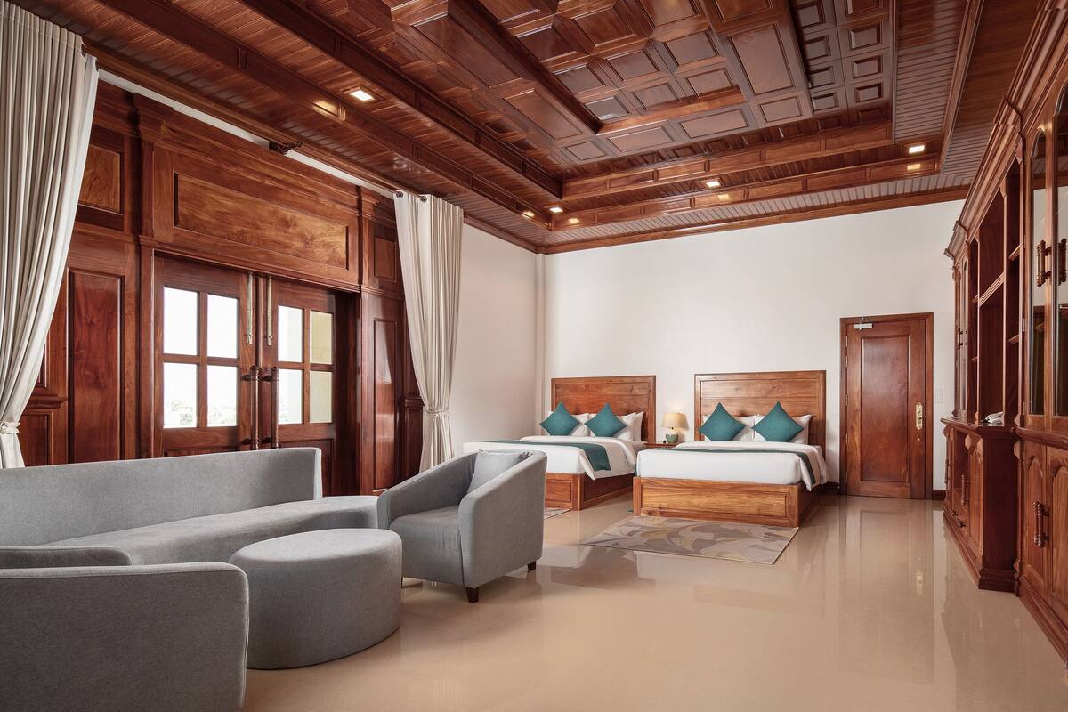 A spacious bedroom with two beds, a large grey sofa, and wooden paneling on the ceiling.