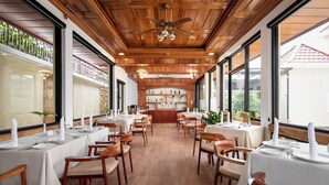 Un restaurant avec un plafond en bois et de grandes fenêtres, des tables dressées pour le service et une cuisine visible au fond de la salle.