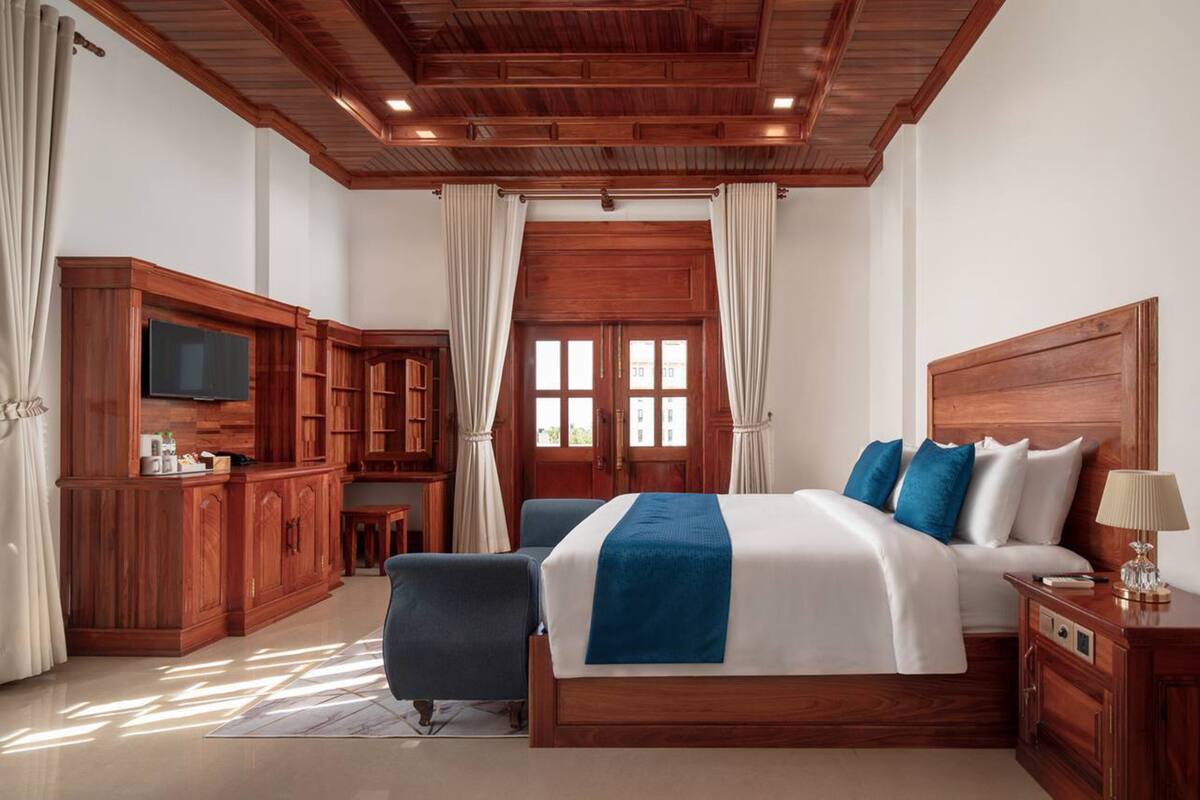 A hotel room with a wooden ceiling, a large bed with blue and white bedding, a TV on a wooden cabinet, and a desk with a chair.