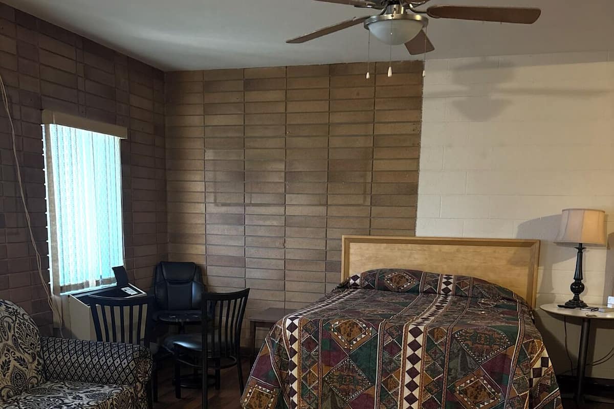 A bedroom with a bed, a desk, a chair, a sofa, and a ceiling fan.